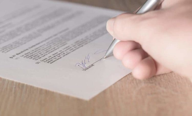 Persons hand writing a signature on a piece of paper