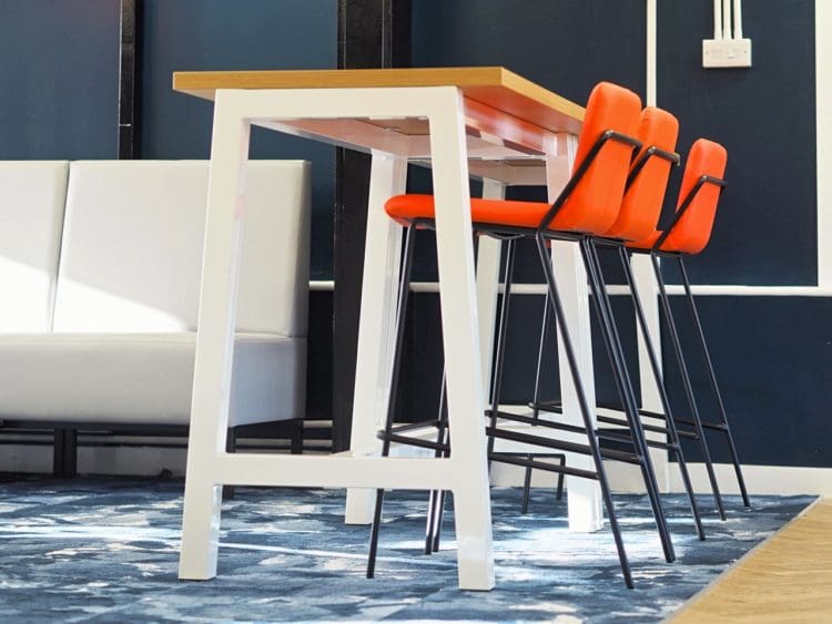 A high poseur table with oak top and white frame and bar stools for school canteen breakout space for sixth form students