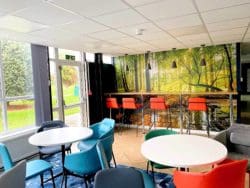 Soft seating options in a sixth form coffee shop area with low café chairs and round tables and a high bar style bench and bar stools.