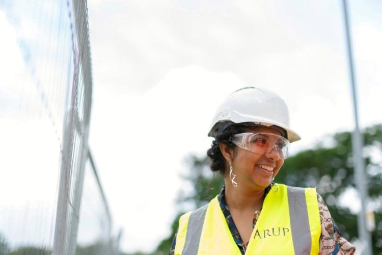 A woman working in construction smiling with a white hard hat