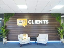 Feature wall in office reception area with light up company logo sign, faux plant corners and soft seating