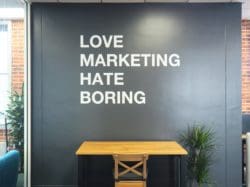 An inspiring quote wall mural on a black wall in an industrial inspired workspace interior design for a marketing agency