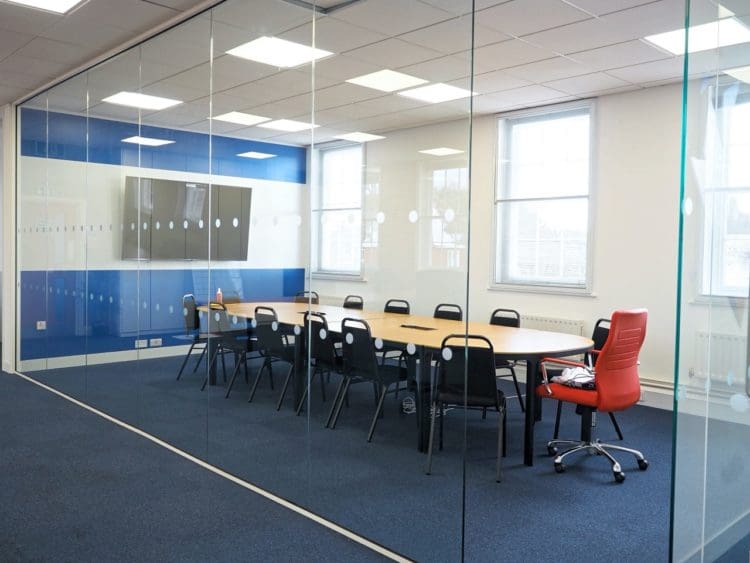 A large office meeting room with a glass partition to separate it from the open plan office with meeting room furniture