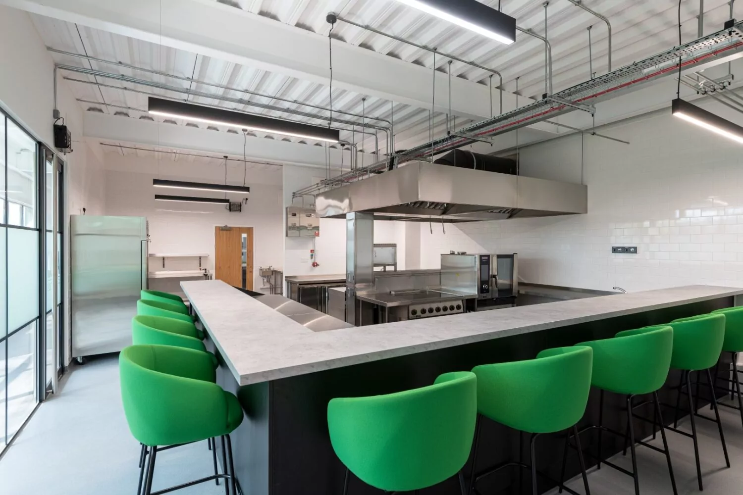 Green poseur height stools and anthracite bar in a commercial tasting kitchen in Kent.