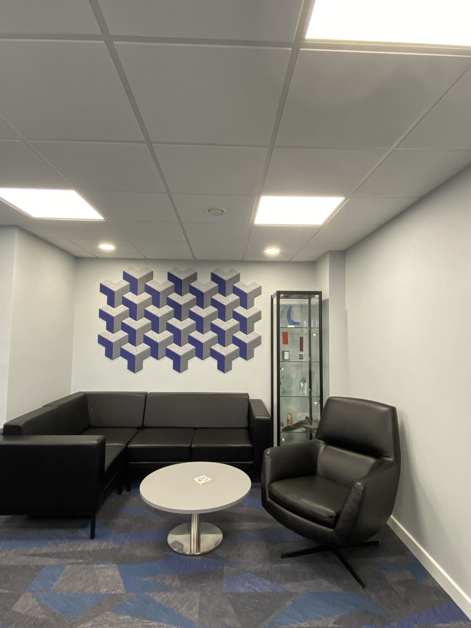 Office breakout area including black leather seating and chrome details with acoustic wall panels featured behind.