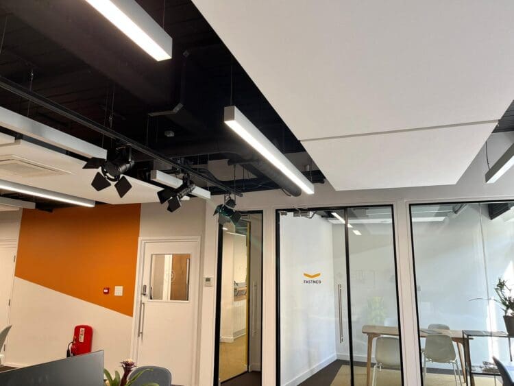 Black exposed ceiling with modern lighting and white acoustic ceiling panels.