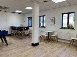 Large office breakout area design with dining furniture and wood effect flooring.