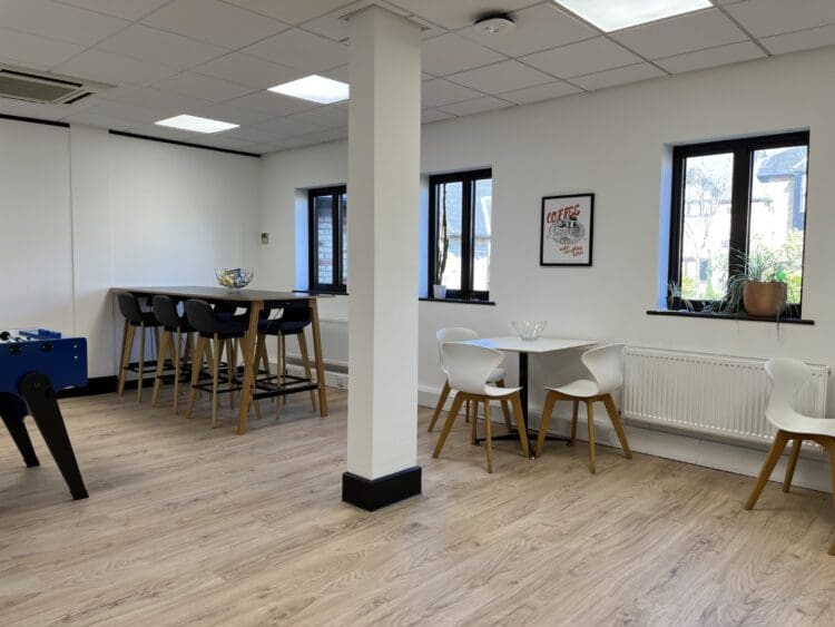 Large office breakout area design with dining furniture and wood effect flooring.